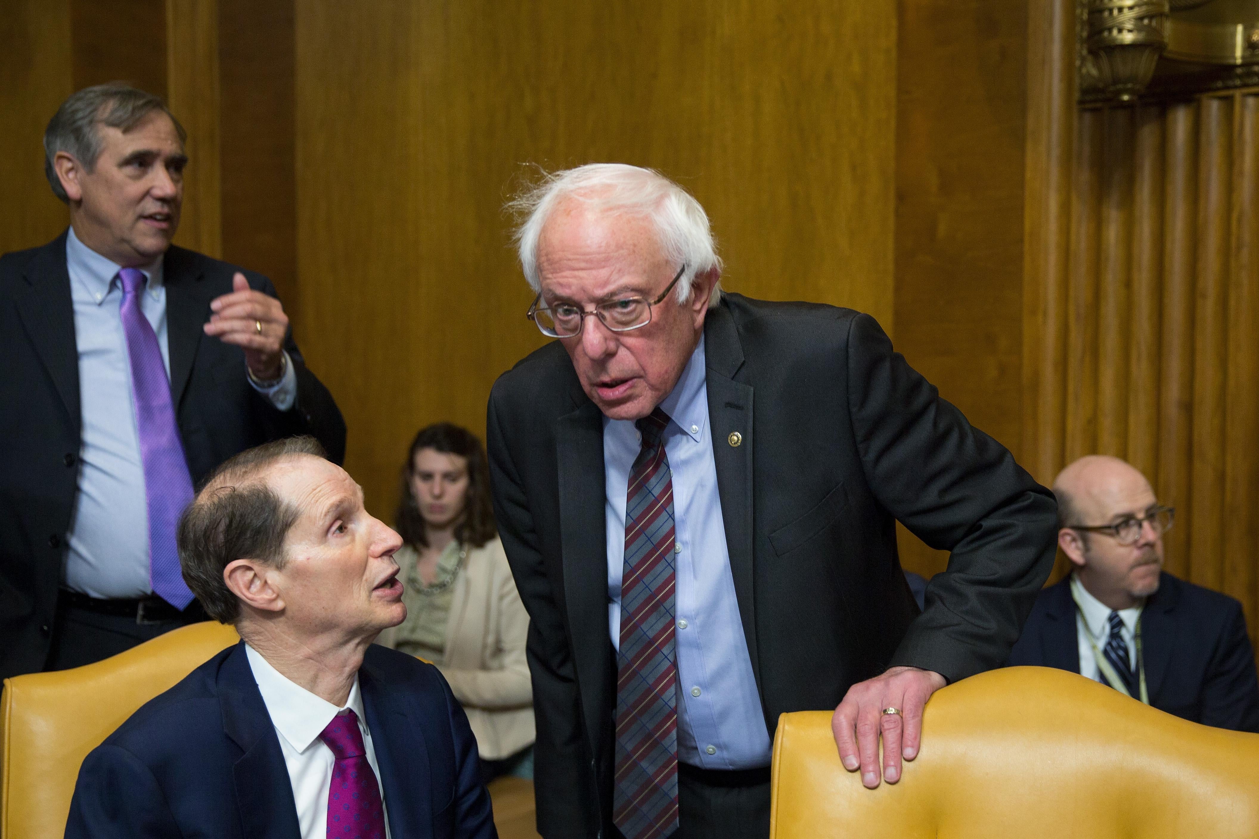 Ron Wyden speaks to Bernie Sanders, who looks quizzical, during a committee meeting