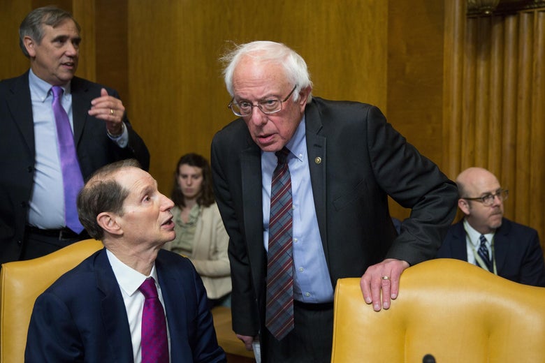 Ron Wyden speaks to Bernie Sanders, who looks quizzical, during a committee meeting