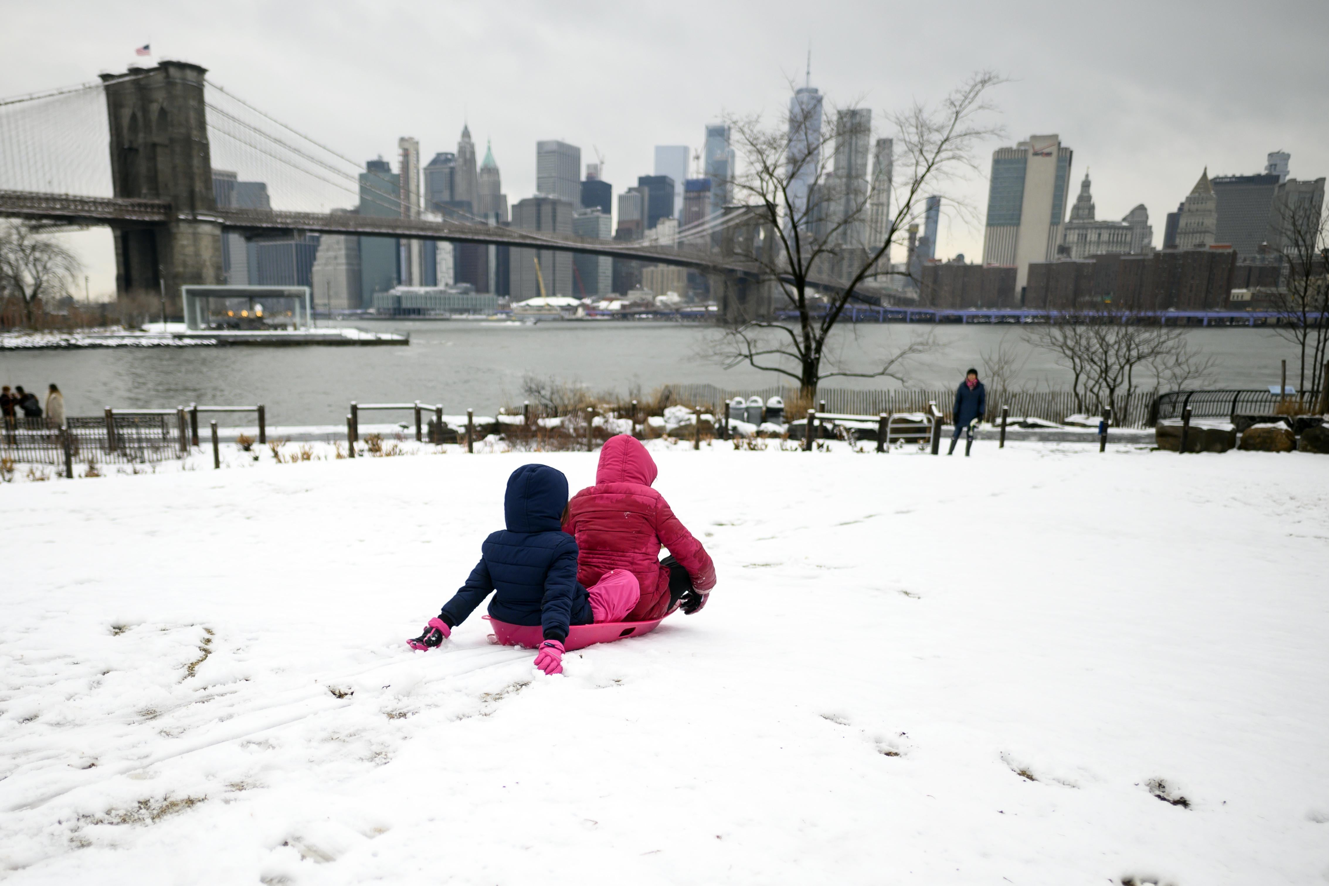 Two girls ride a sled on a snow-covered hill in New York.