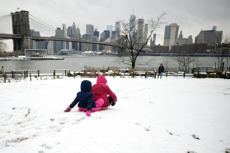 Two girls ride a sled on a snow-covered hill in New York.