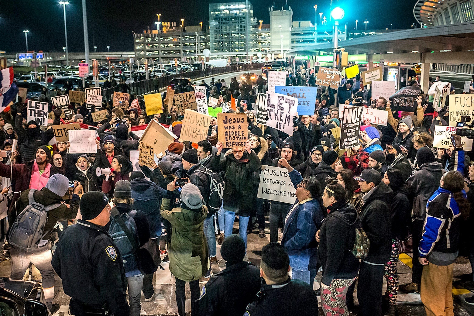 People hold up signs against the Muslim ban outside the terminal at night.