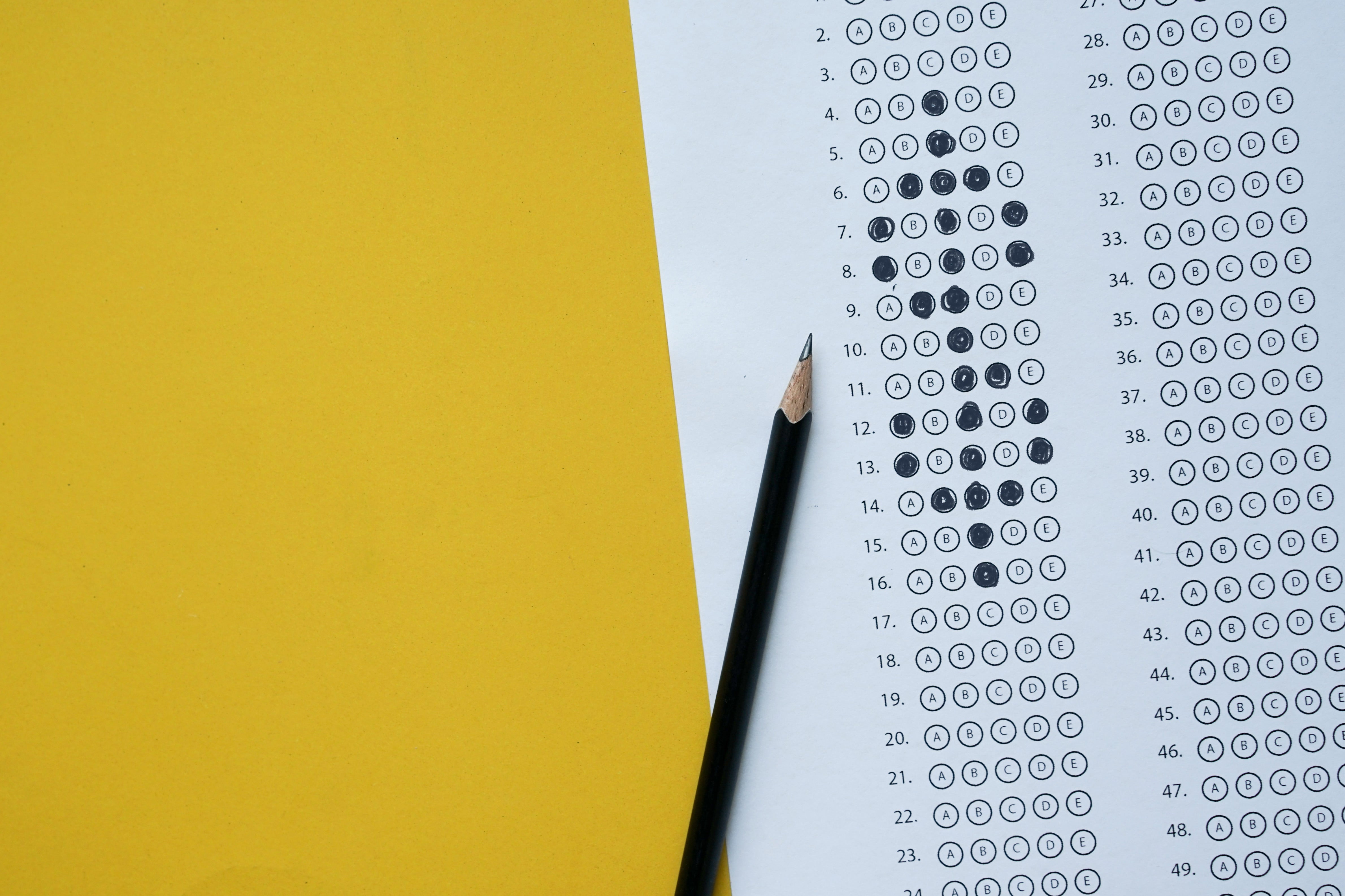 A partially filled-in scantron and pencil over a bright yellow background.