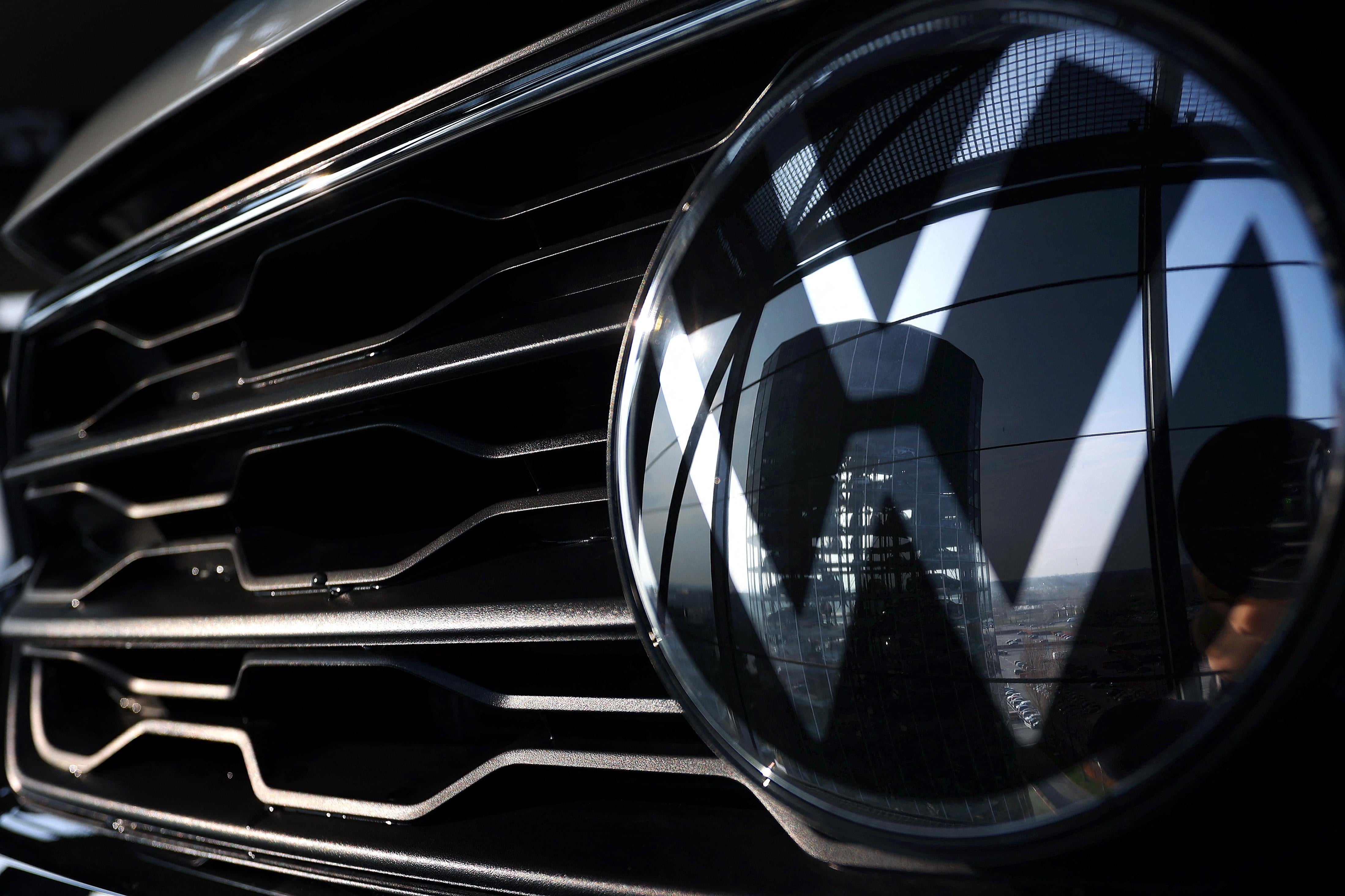 A VW logo reflecting a building is seen on the grille of a car.
