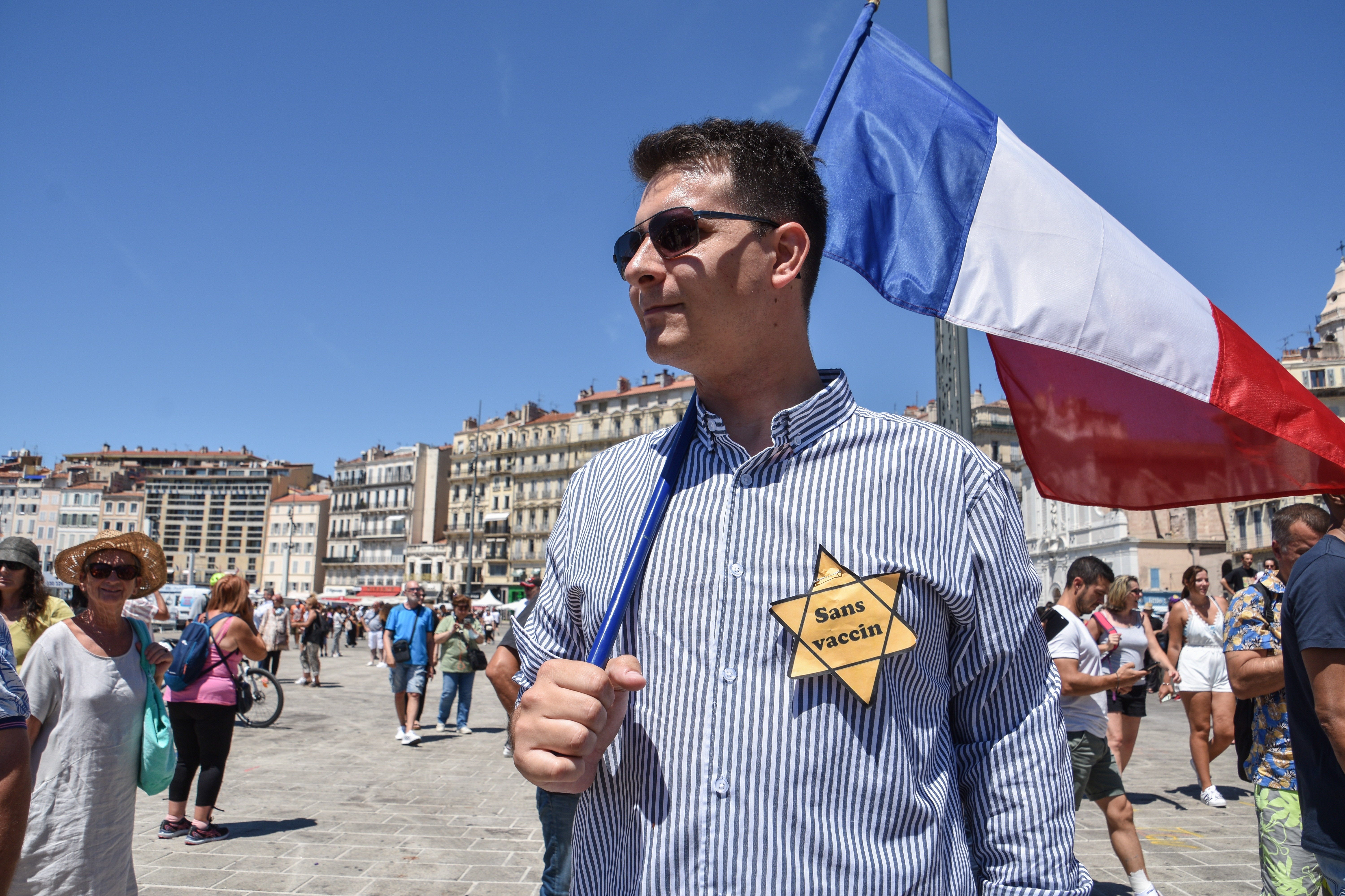 Man in sunglasses holding a French flag and wearing a yellow star reading "sans vaccin."