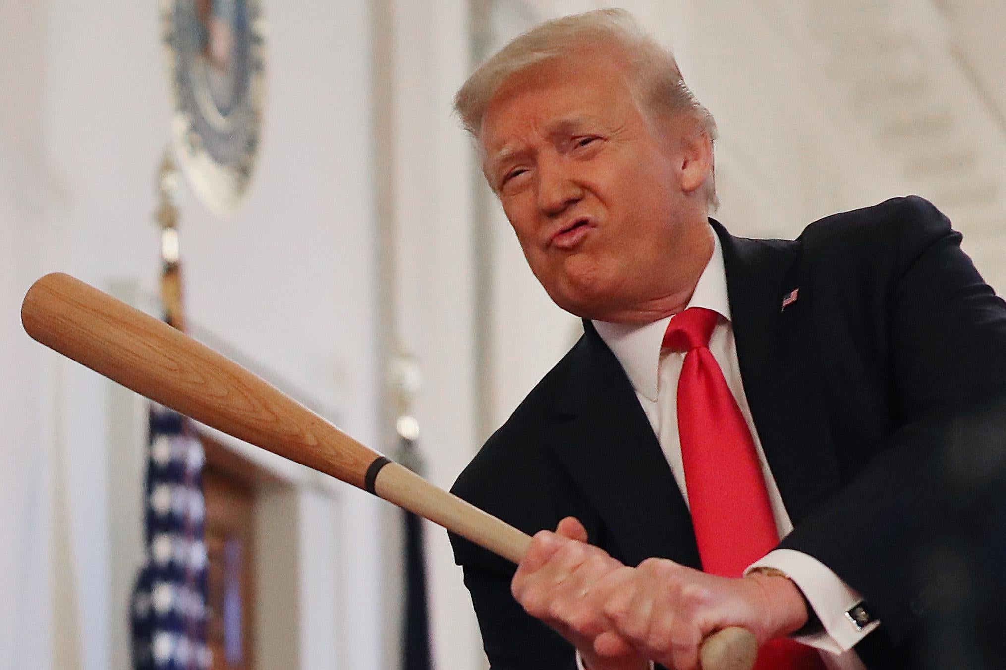 Donald Trump grimaces as he swings a baseball bat.