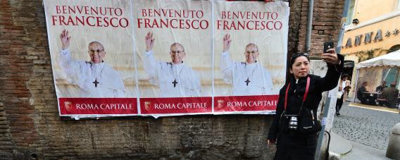 A woman poses in front of posters of Pope Francis on March 15, 2013, near St Peter's Square at the Vatican.