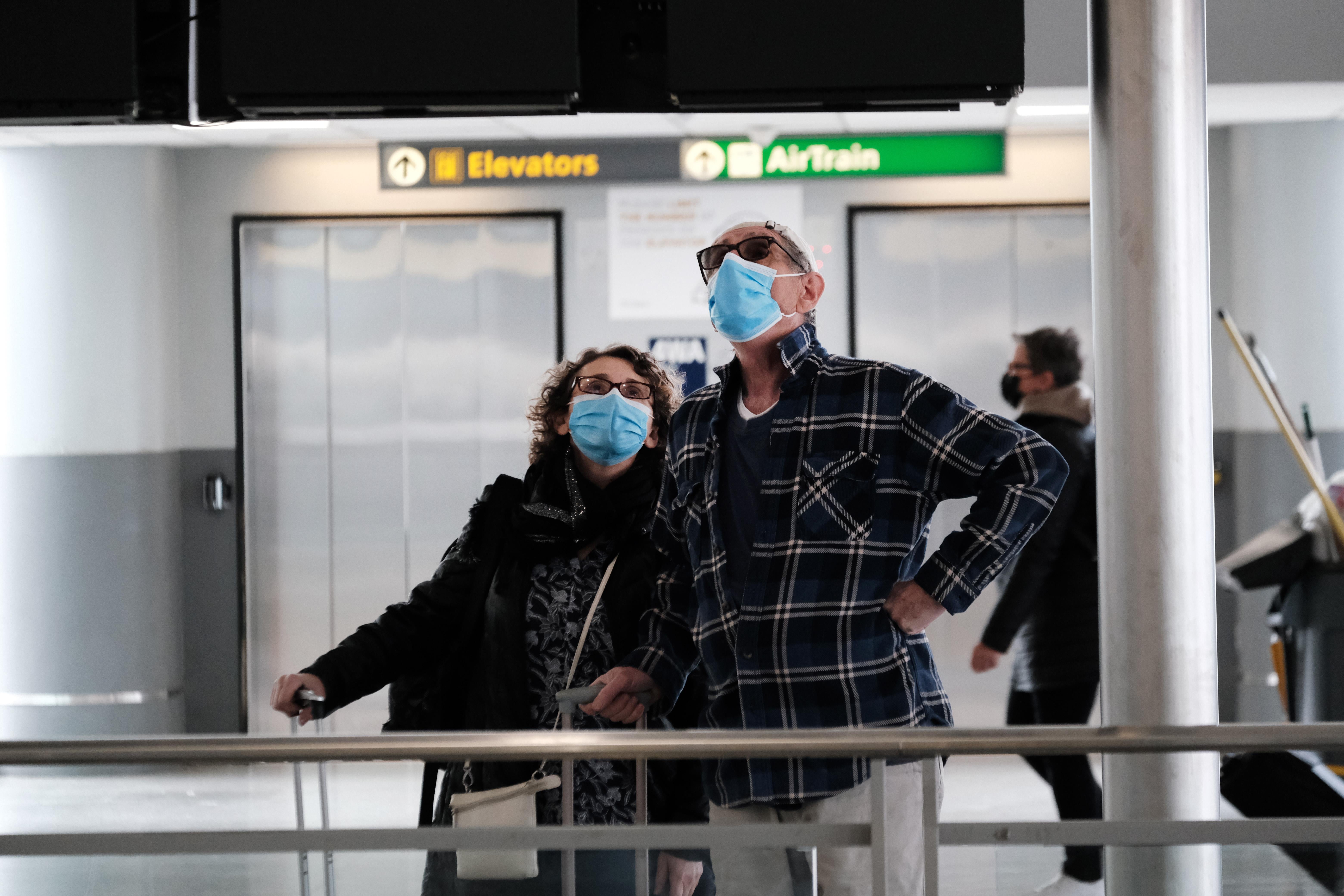 Two people in an airport wearing masks look up at a screen.