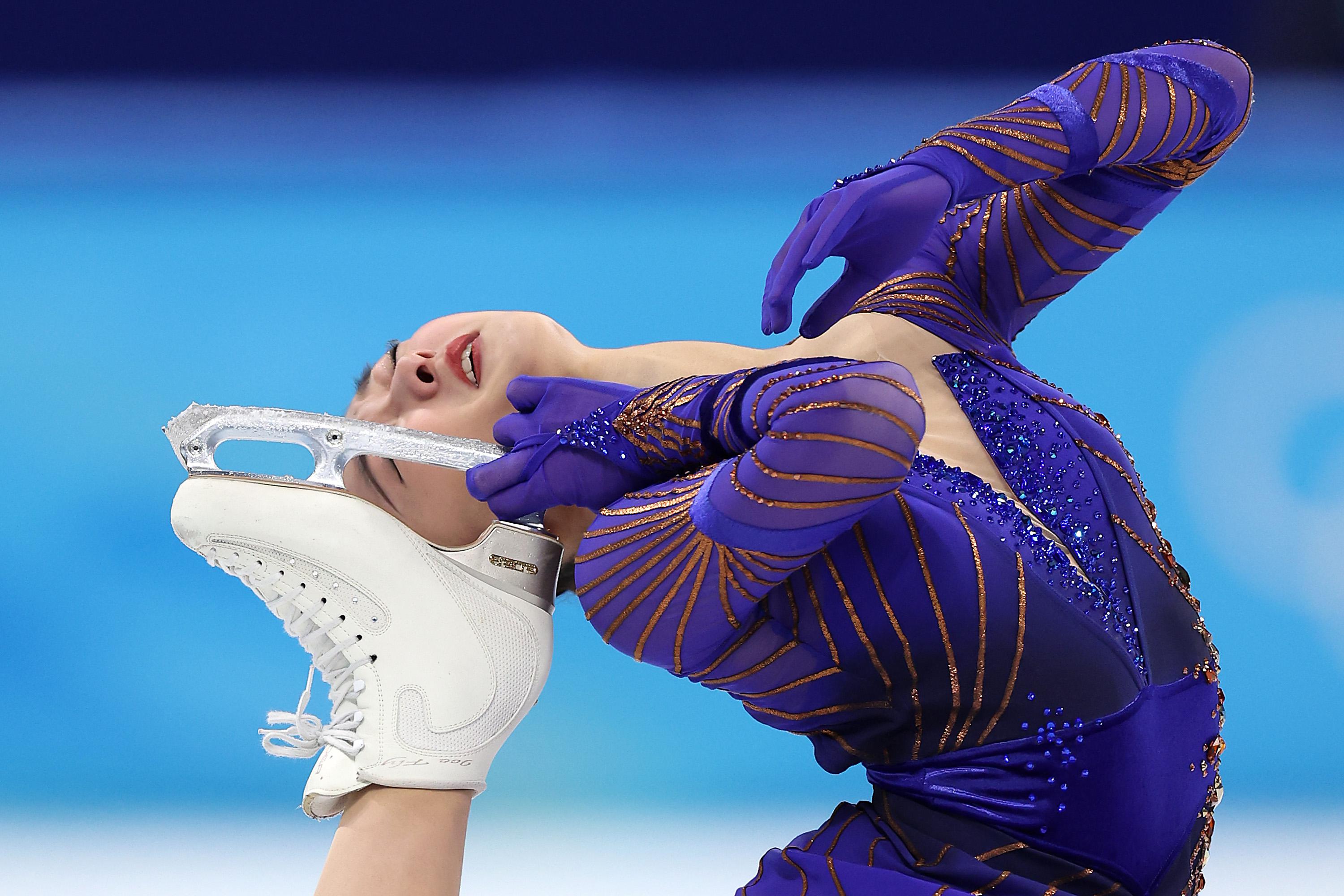 Sakamoto lifting her skate behind her head and leaning backward with her eyes closed on the ice