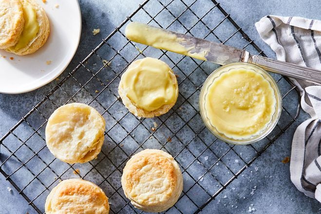 Biscuits on a cooling rack with a small container of corn butter. A smeared knife is next to one buttered biscuit.