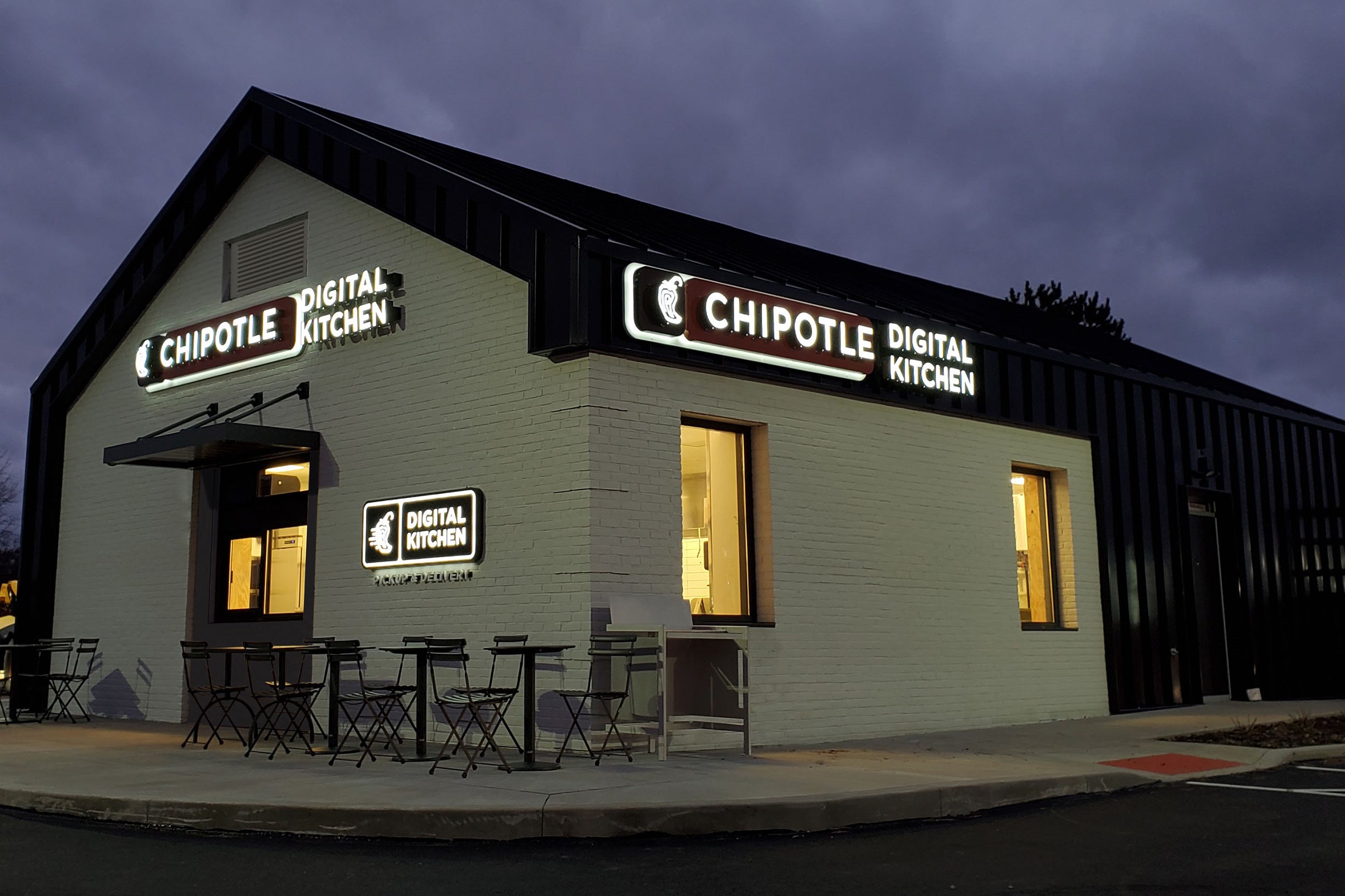 The exterior of a tiny Chipotle store. Free-standing. At night.