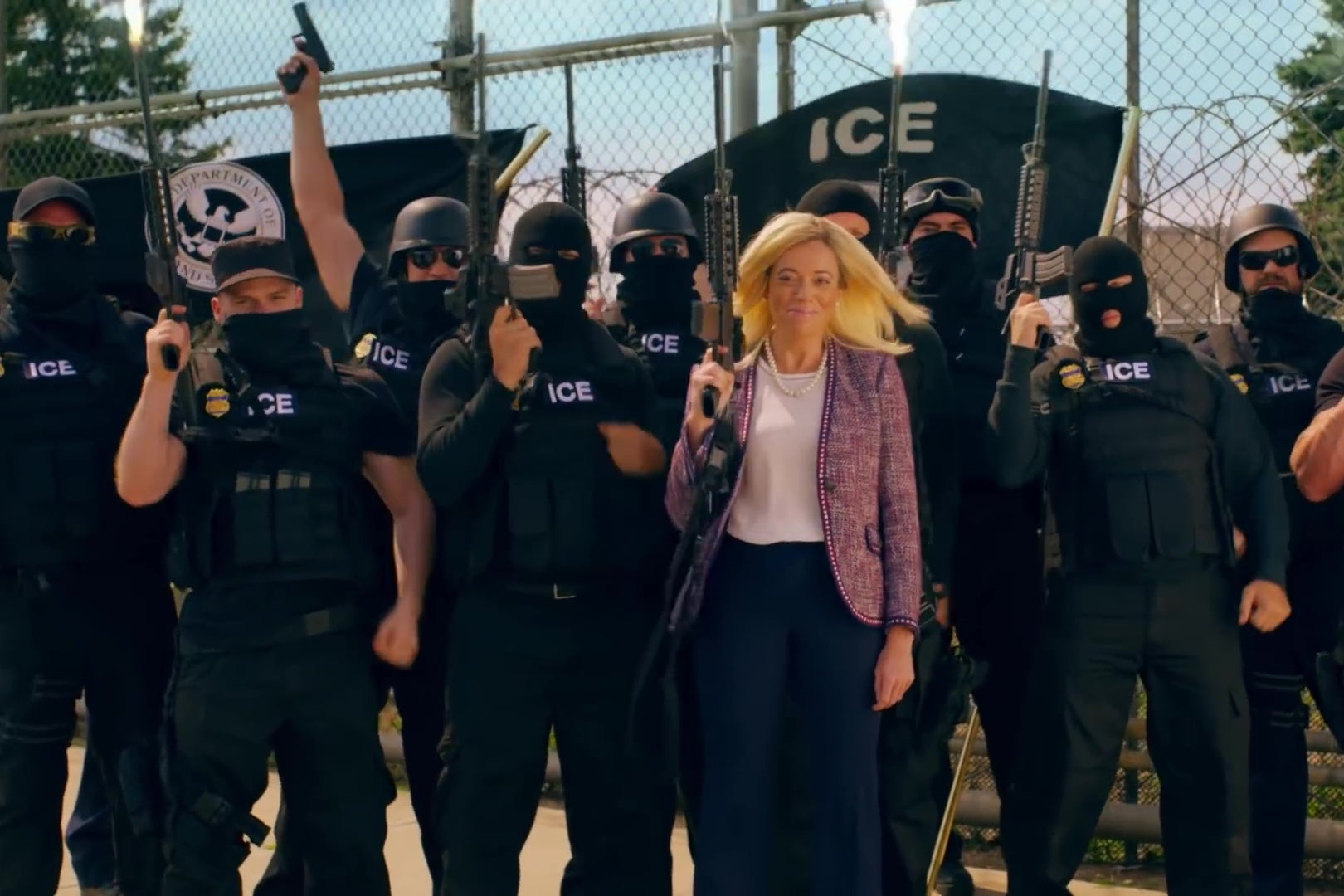 Michelle Wolf stands in front of a group of black-clad ICE agents holding automatic weapons.
