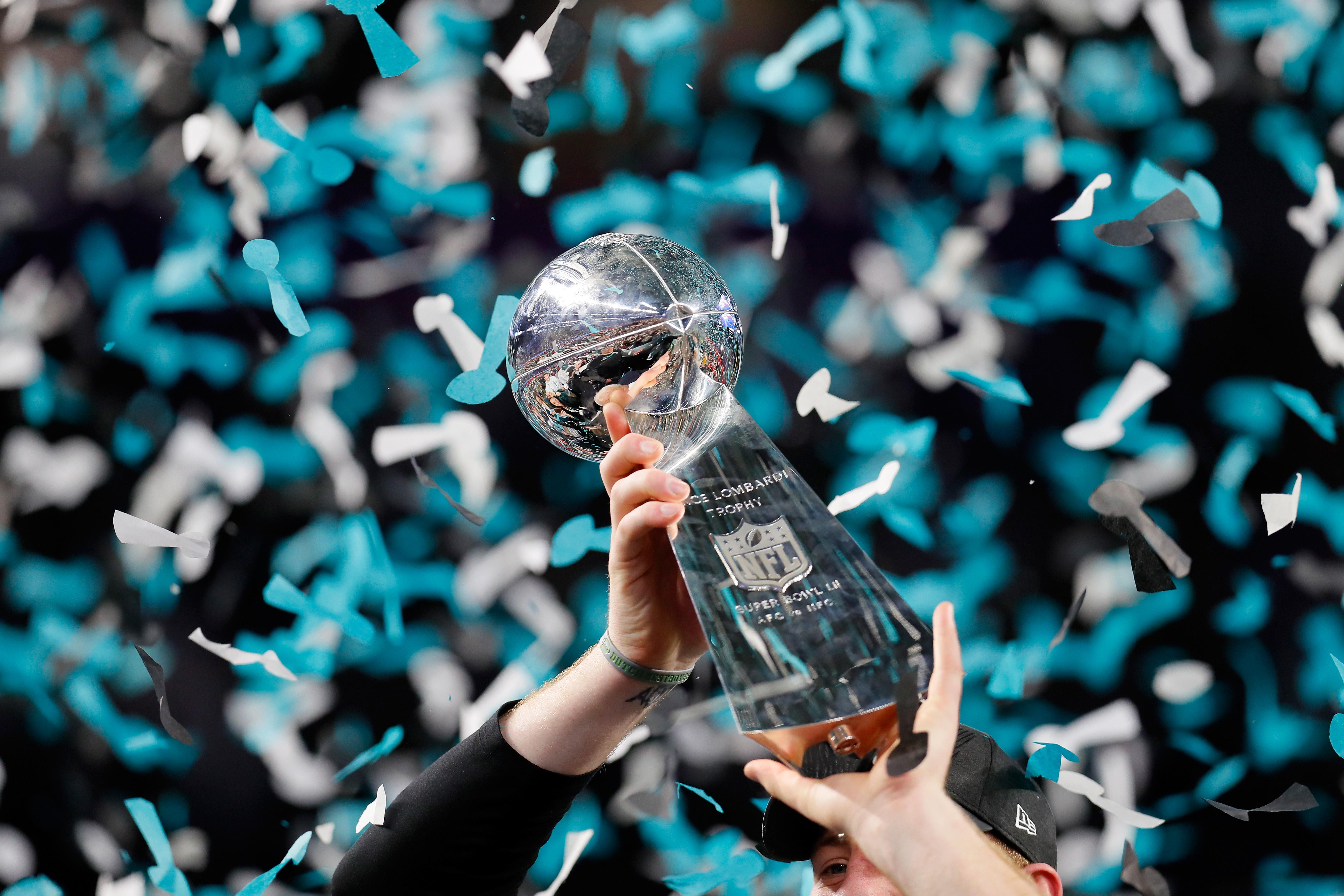 The Vince Lombardi Trophy is held in the air as confetti falls.
