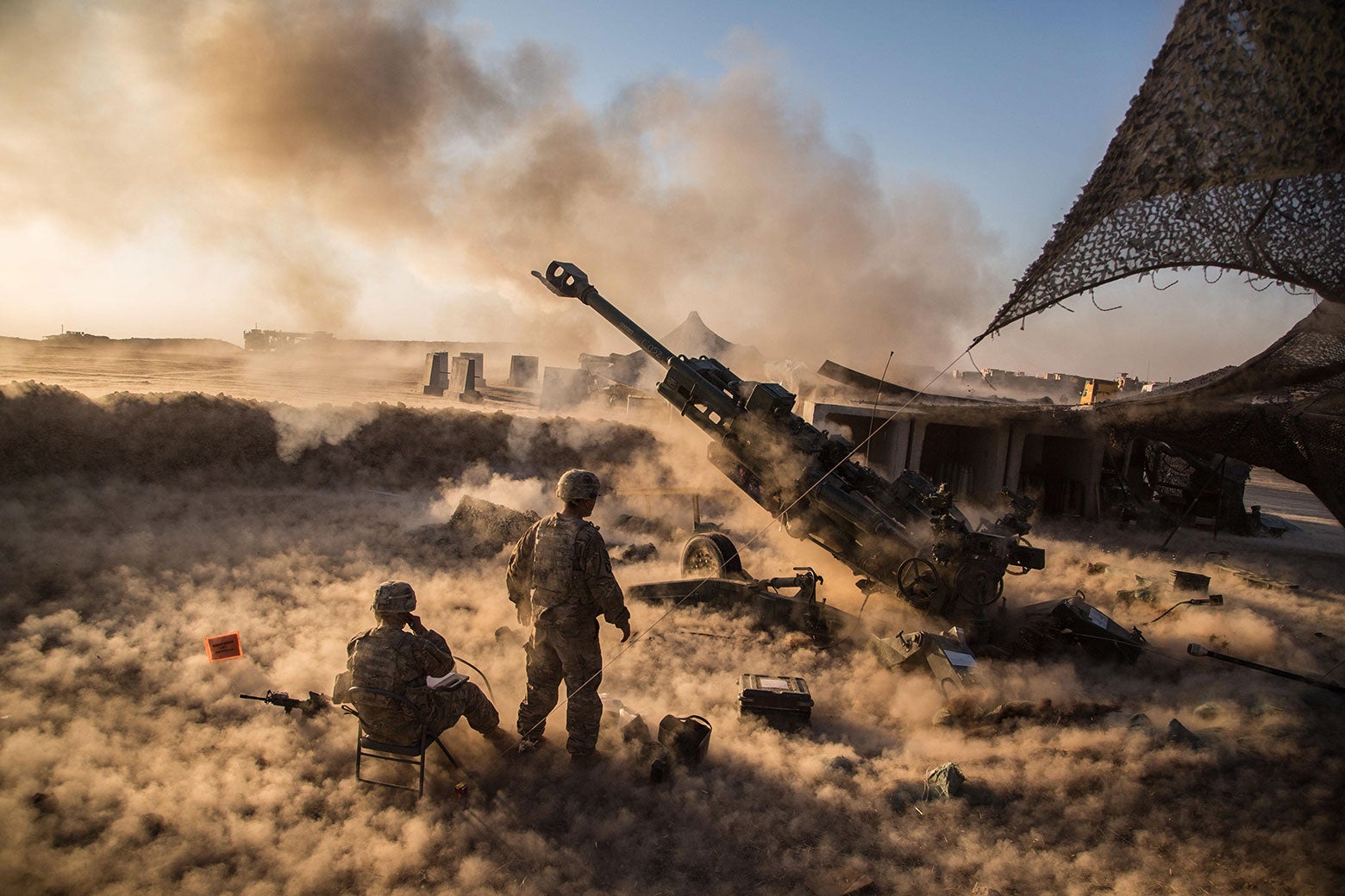 Two soldiers stand next to a smoking cannon as sand swirls around them dramatically. 