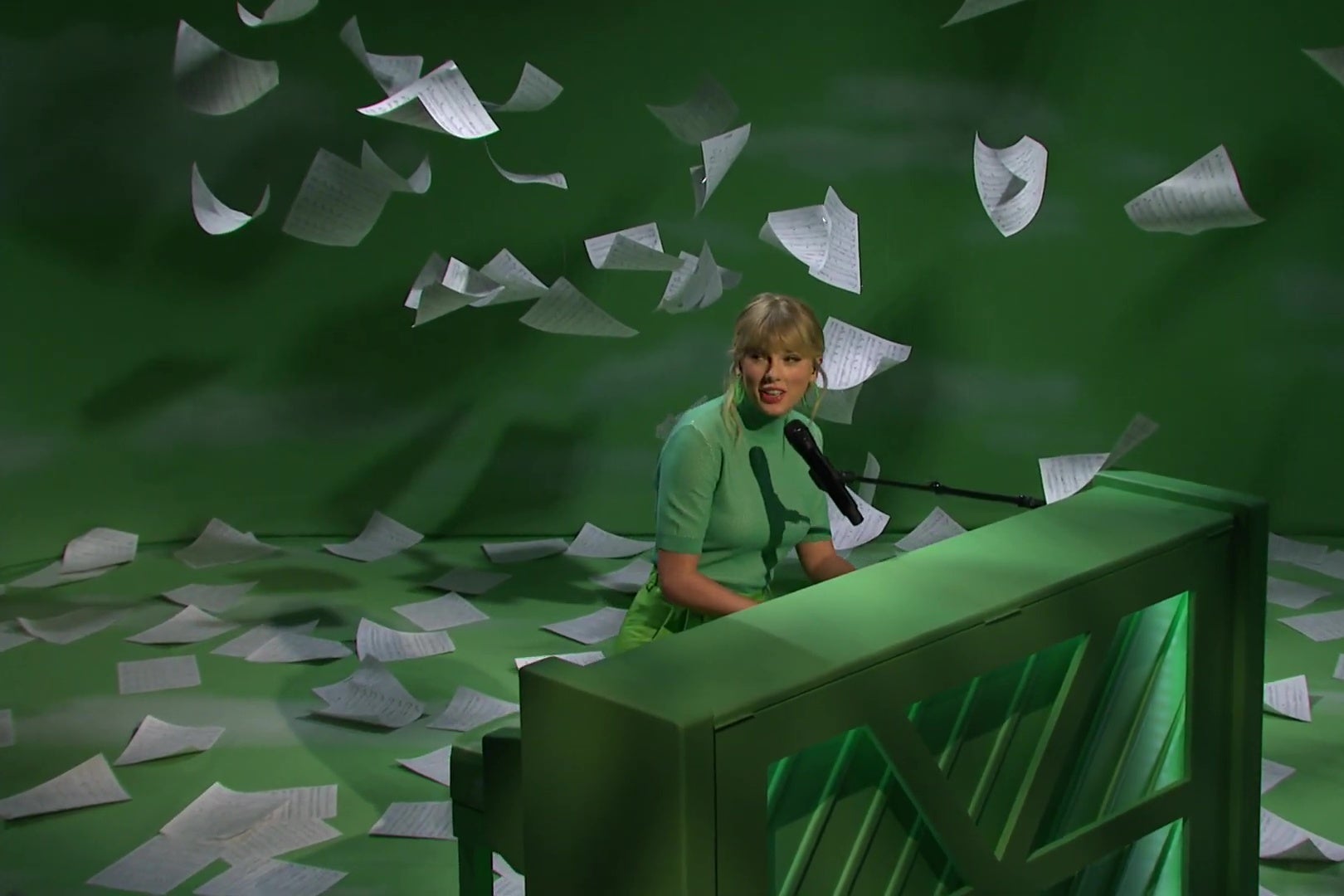 Taylor Swift plays a green piano on a green stage.