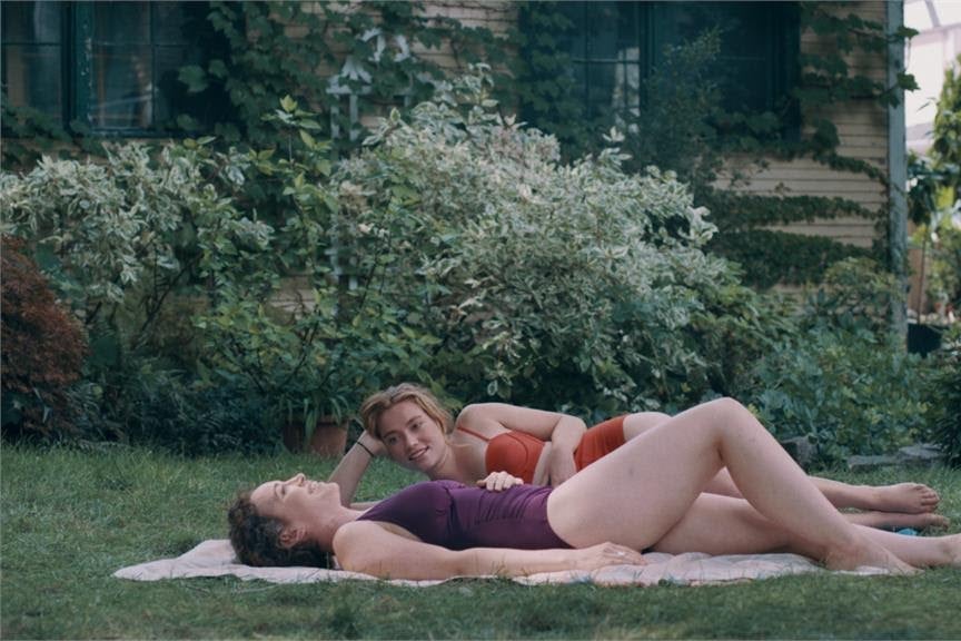 Jessie Pinnick and Rebecca Spence lounge on a blanket in the grass wearing bathing suits.