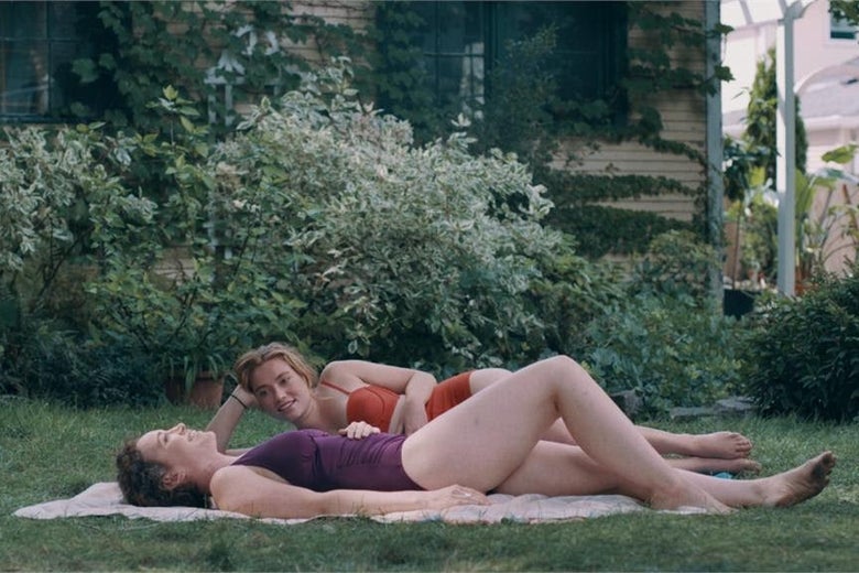 Jessie Pinnick and Rebecca Spence lounge on a blanket in the grass wearing bathing suits.