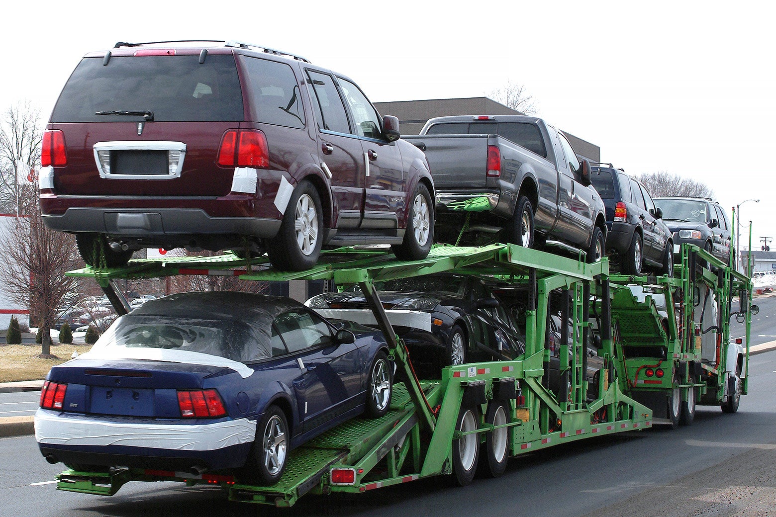 A green auto hauler carries eight vehicles, from sedans to SUVs to large trucks.