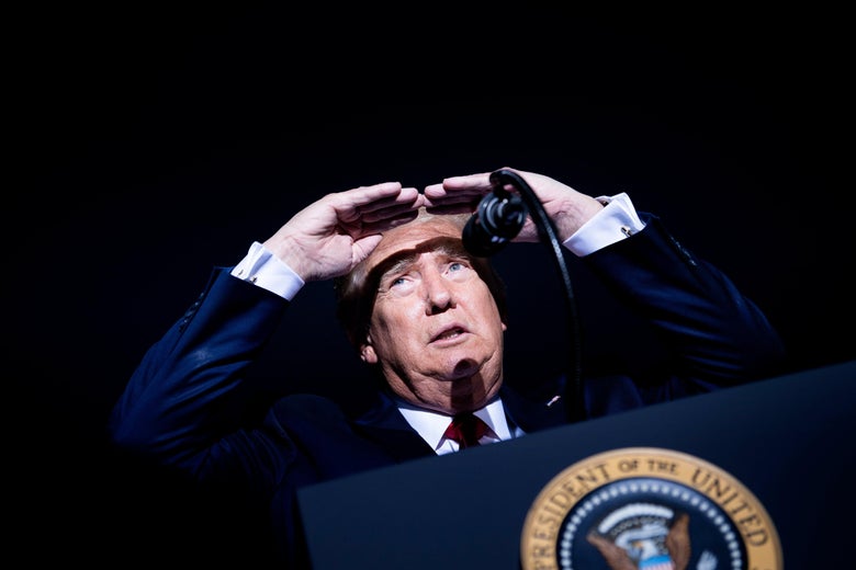Trump shields his eyes from bright lights as he looks out at the crowd at night