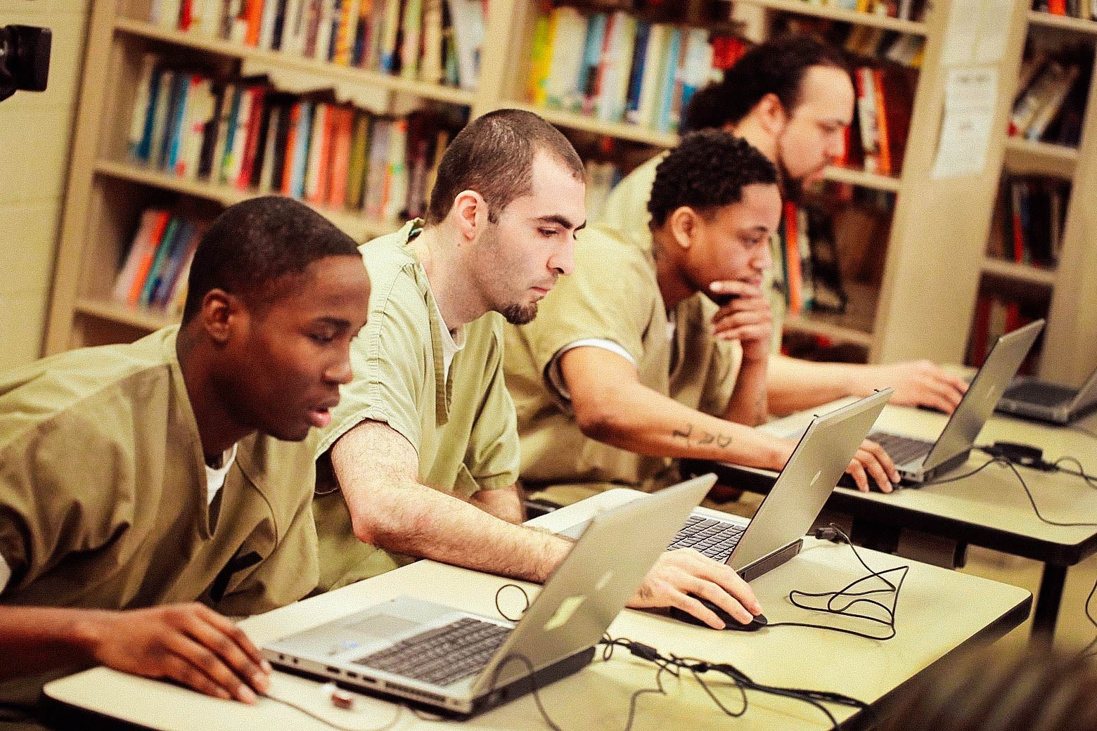 Inmates sit at library desks and work with laptops.