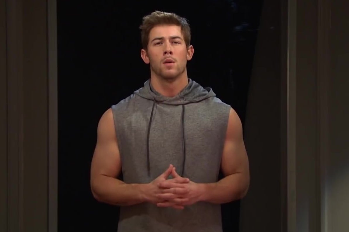 Nick Jonas, in a sleeveless hoodie, flexing.