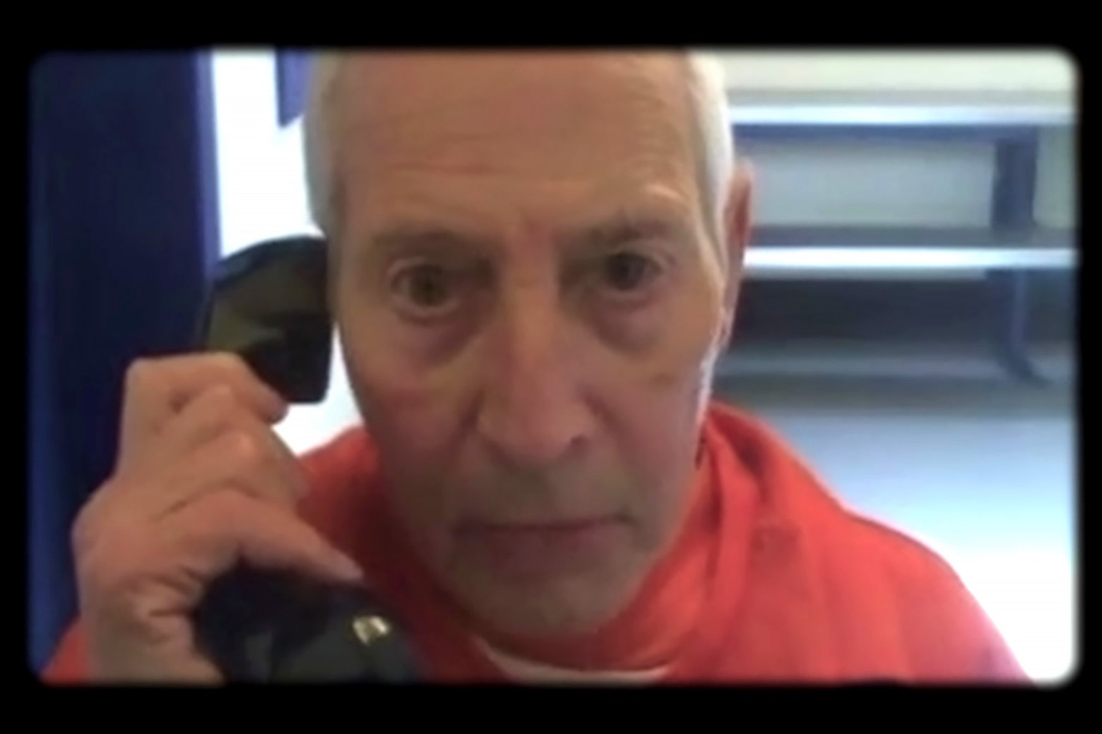 Robert Durst speaks on a prison phone and wears an orange jumpsuit in a scene from the docuseries.