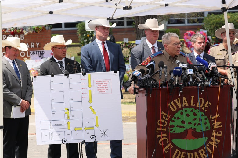 McCraw stands at a podium in front of a bunch of law enforcement officers wearing cowboy hats and a drawn plan of the school where the massacre took place.