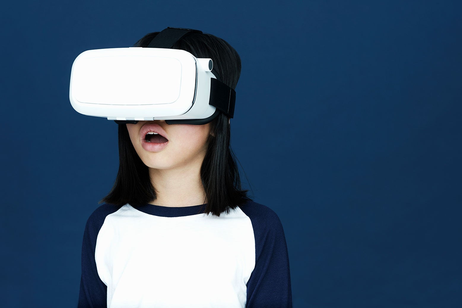 A kid with long hair, opened mouthed, with their head in a VR headset. 