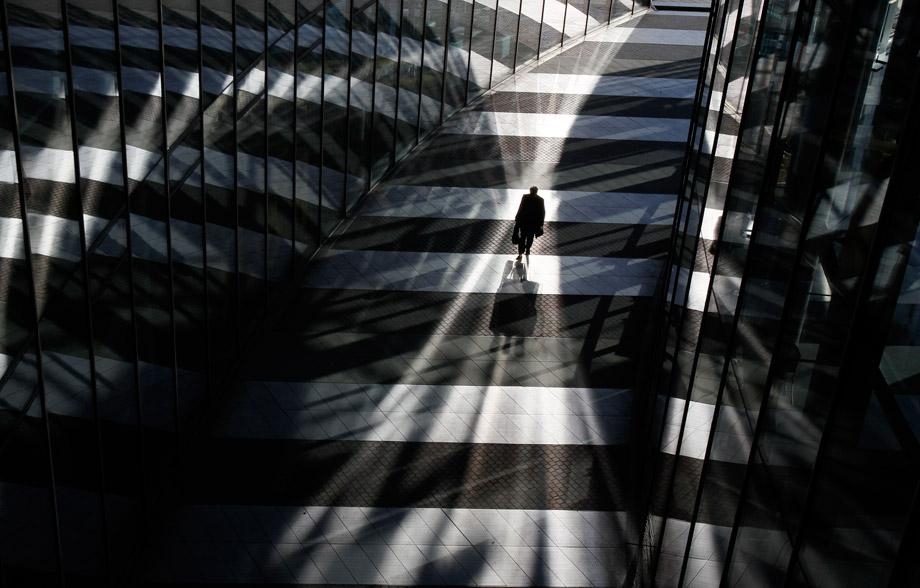 A man walks between glass facades of the Bonn Post Tower, the headquarters of German postal and logistics group Deutsche Post DHL in Bonn March 5, 2013.
