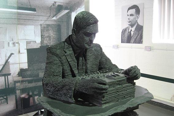 A statue of Alan Turing with his portrait in the background.