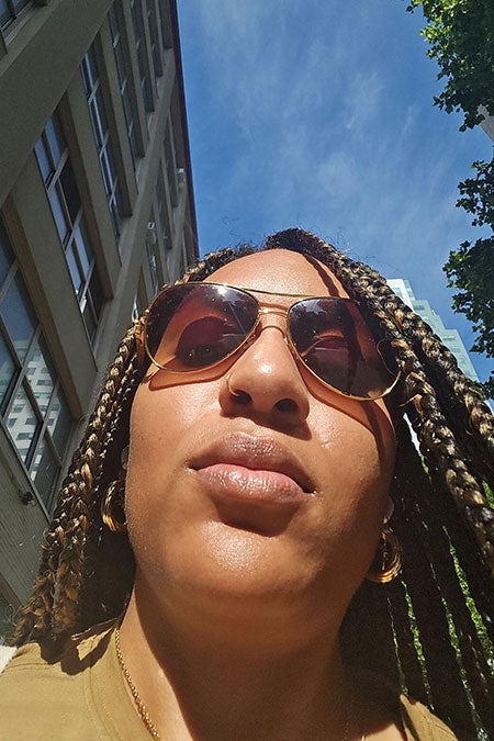 Selfie of the author looking down at her phone while walking down a city street wearing sunglasses and a gold top.