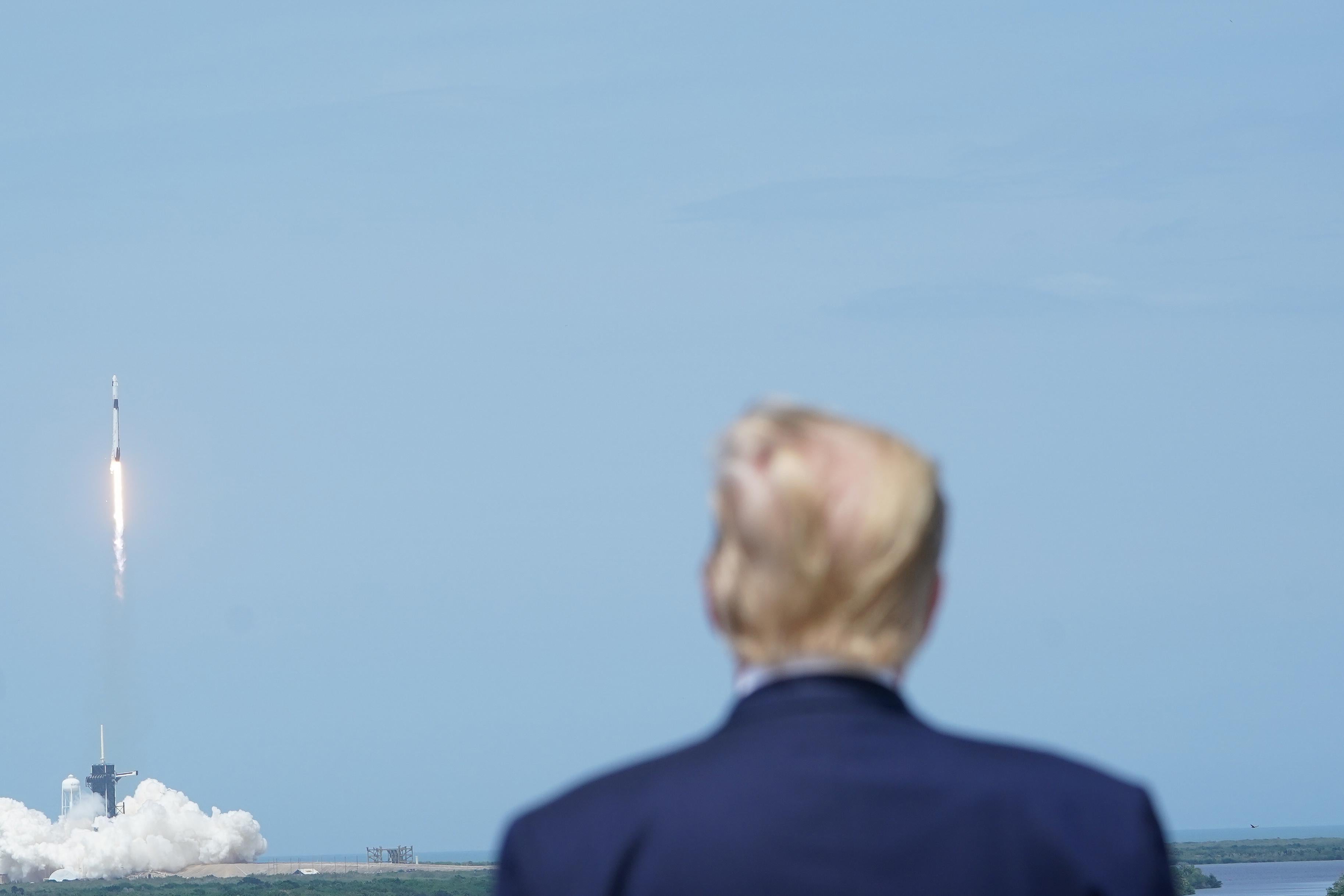 The back of Trump's head can be seen as a spaceship launches in the background.