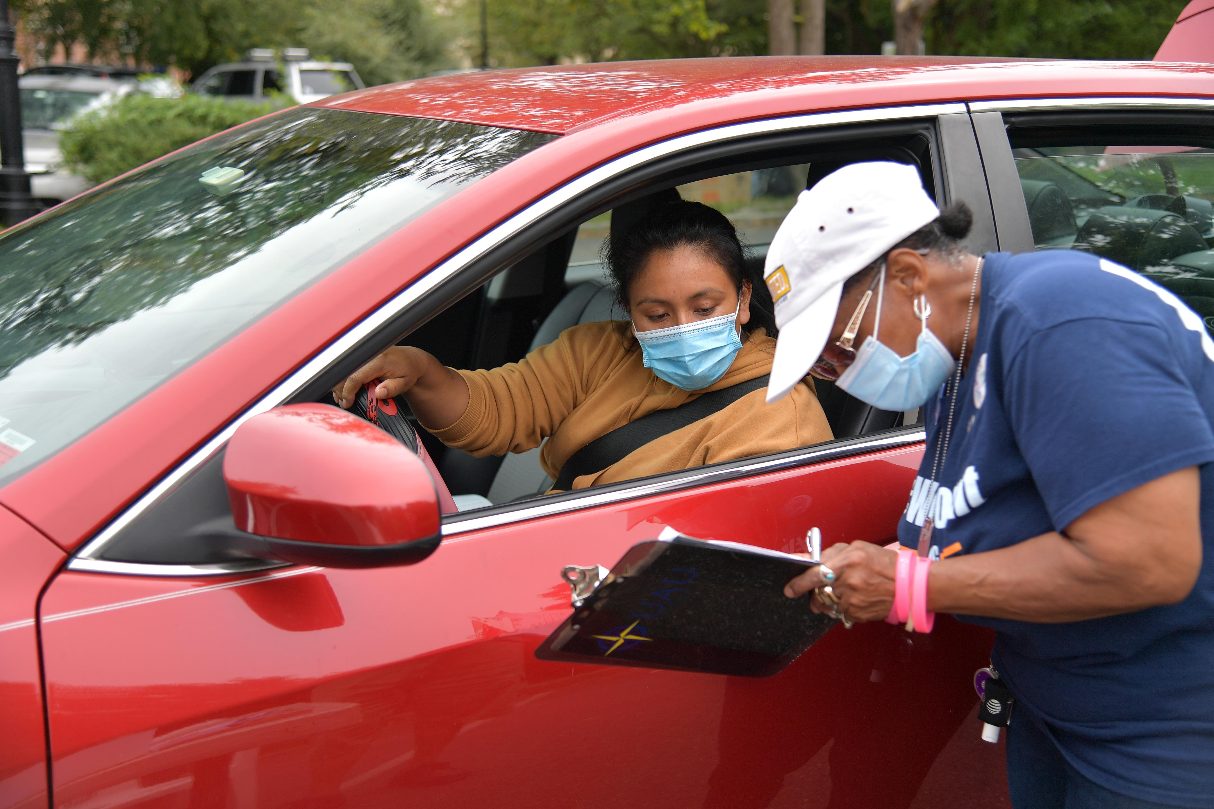 A woman in a face mask fills out a form with another woman in a car