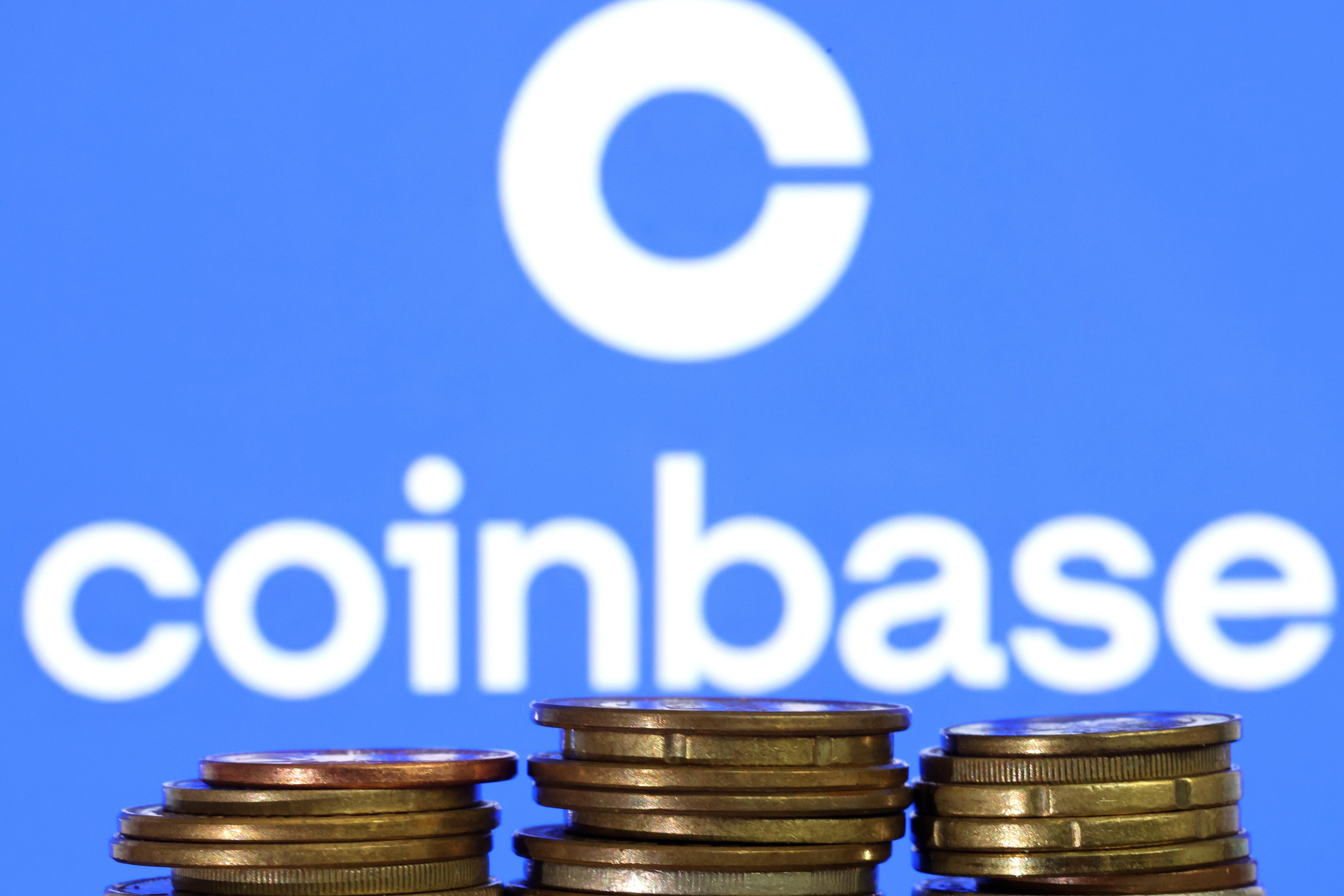 Three stacks of coins seen in front of a screen displaying the Coinbase logo.