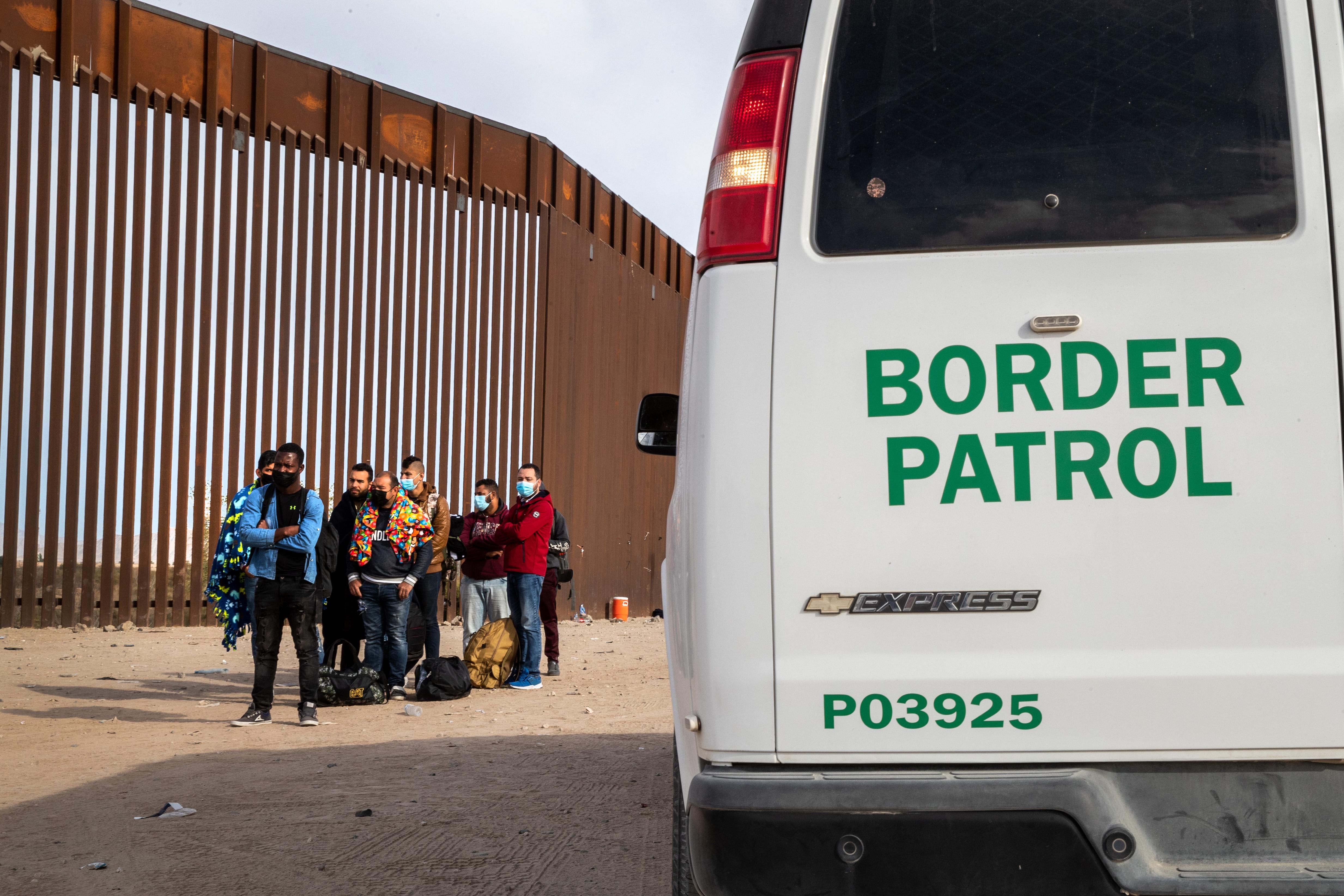 A Border Patrol van next to officers taking migrants into custody