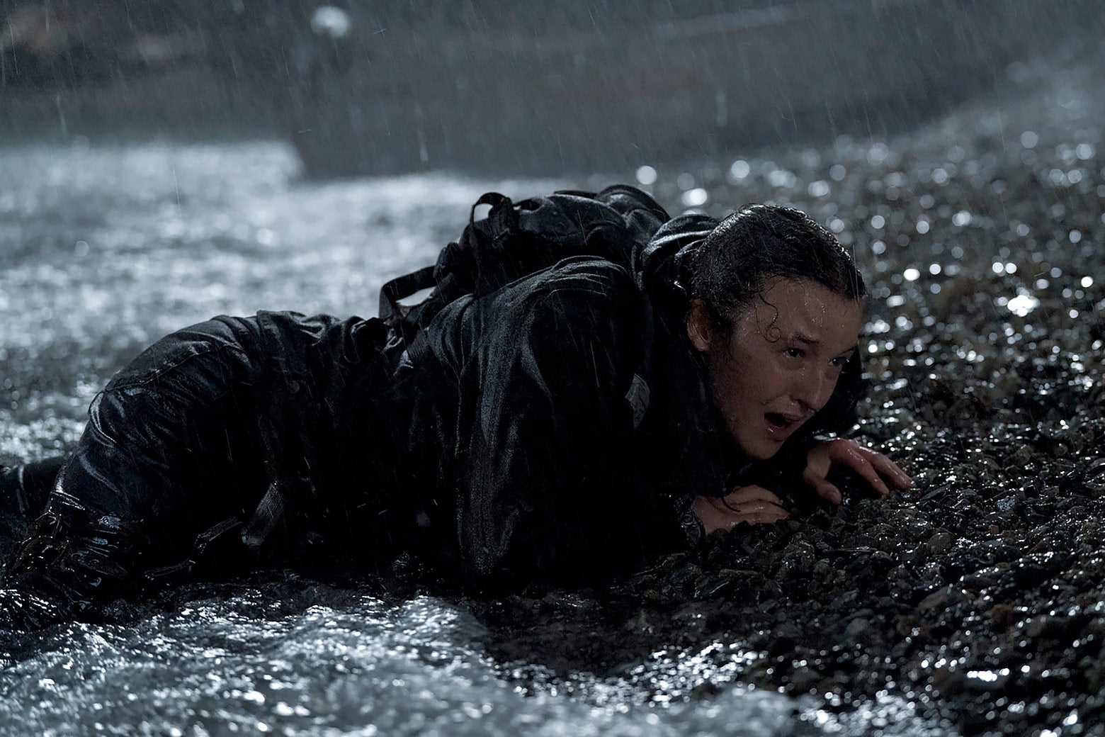 Bella Ramsey lays on the dirty, wet ground in torrential rain.