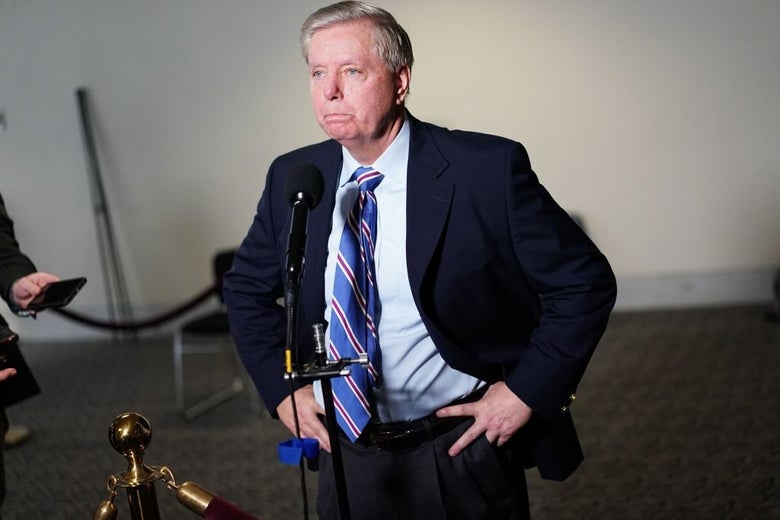 Graham makes a face that conveys resignation as he stands in front of a microphone.