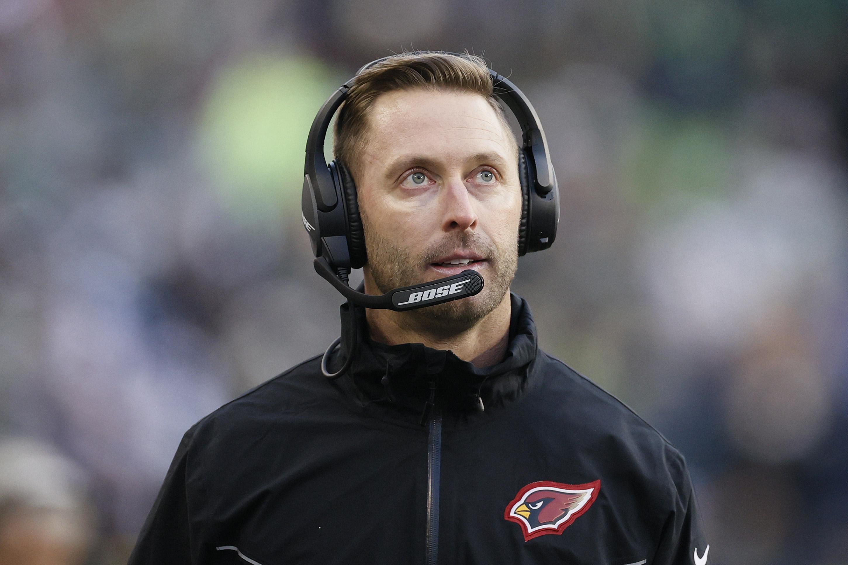 The Cardinals' coach in a headset and team quarter-zip looking upward on the sideline.