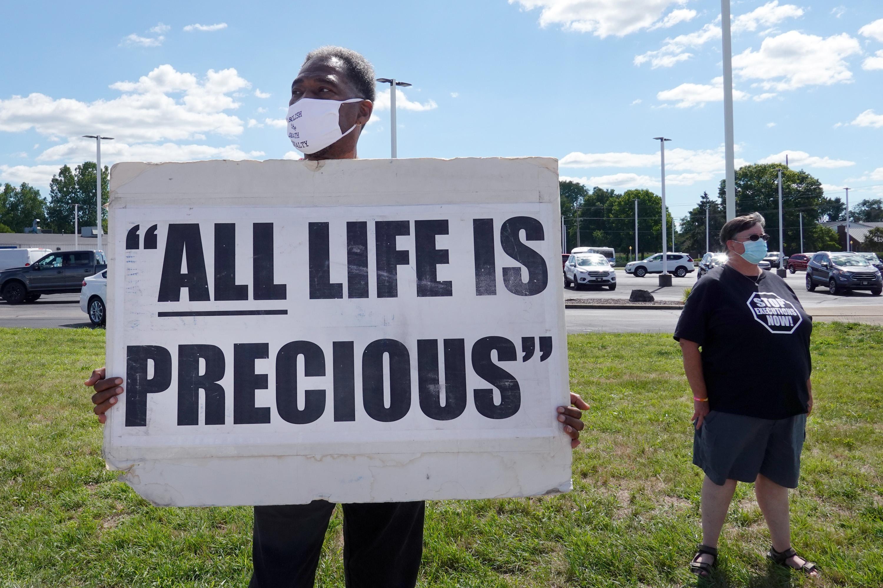 Man holds up sign that says "ALL LIFE IS PRECIOUS."