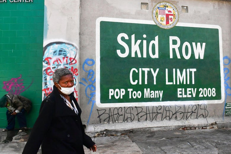 A woman walks past a Skid Row sign pointing out a population of "Too Many."