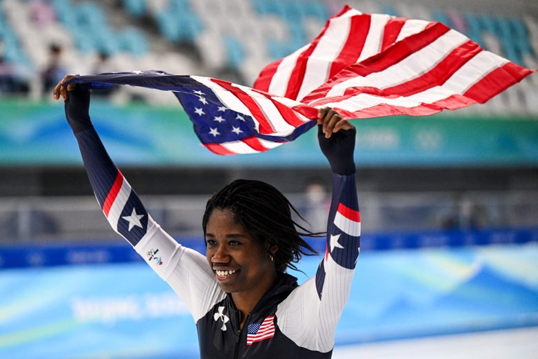 Erin jackson skating, smiling, and carrying an American flag above her head.