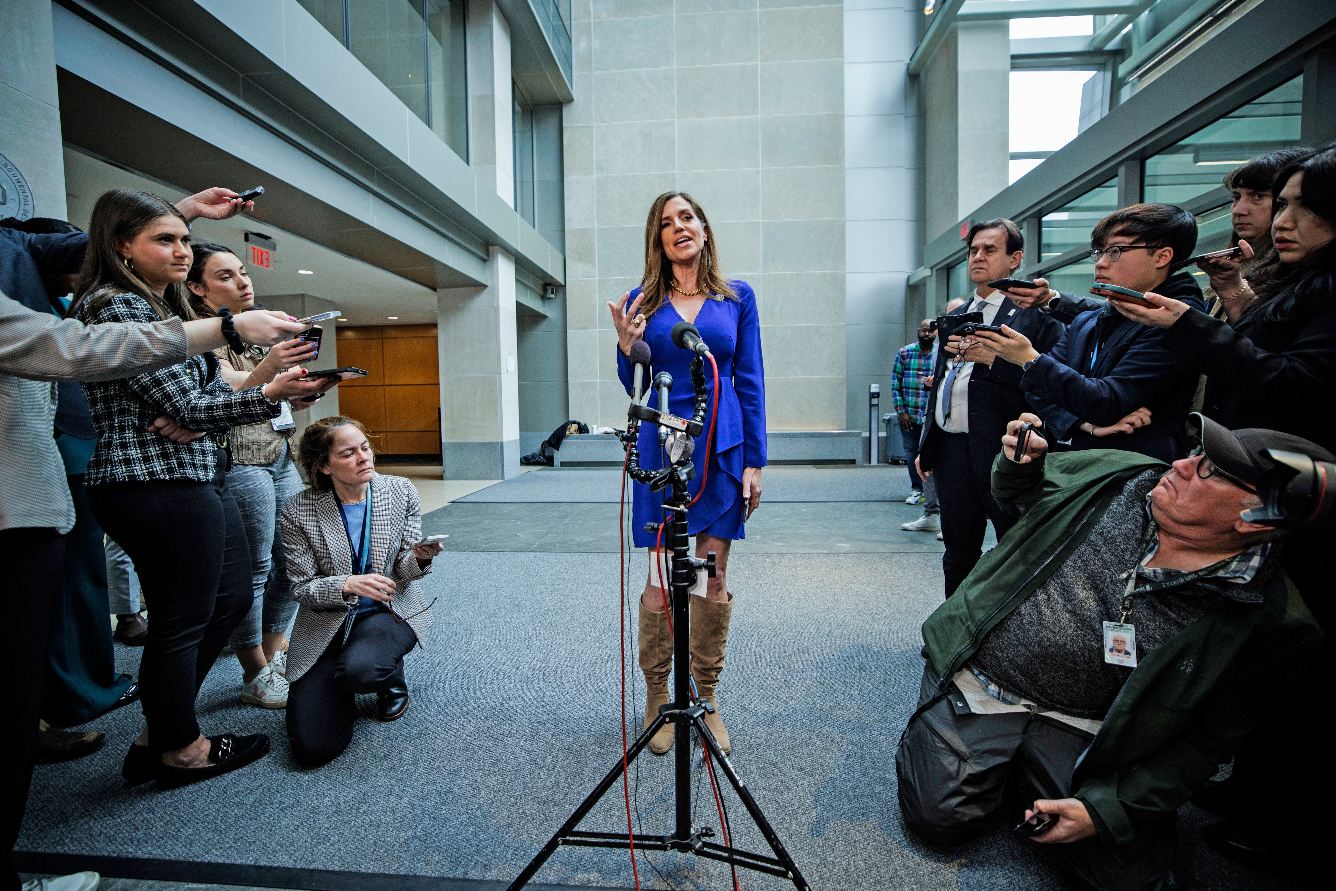 Nancy Mace wears a blue dress and tan boots and and speaks to a group of reporters.