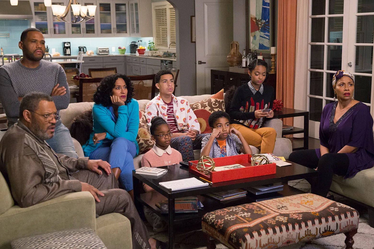 Eight members of a family sit in their living room and watch TV. They look horrified.