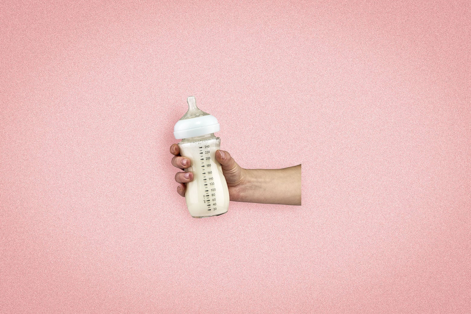 An outstretched hand holding a baby bottle filled with milk, set against a pink background.