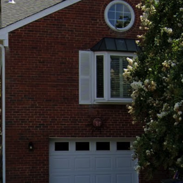 The same house, without the address numbers, but with a yellow sun hanging above the garage door.