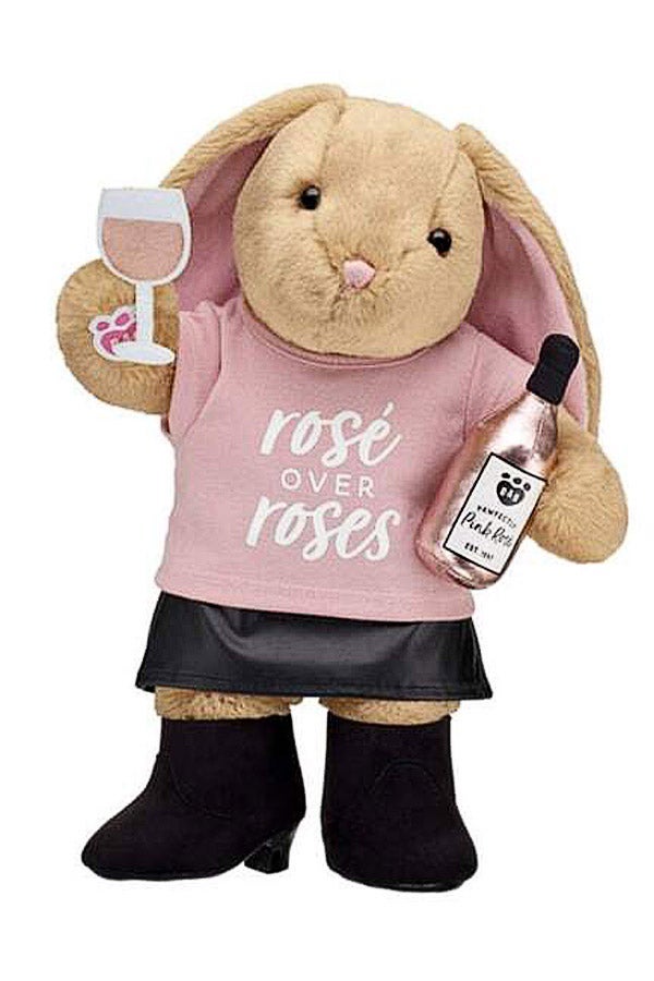 A stuffed bunny in a pink shirt that says "Rosé over roses" holds a fabric glass of wine and a plush wine bottle