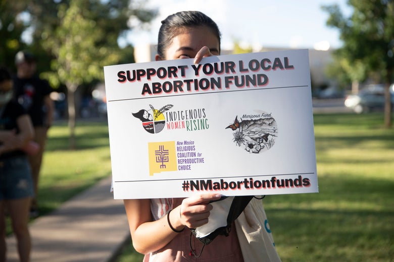 A protester in New Mexico holding a sign that says "Support Your Local Abortion Fund."
