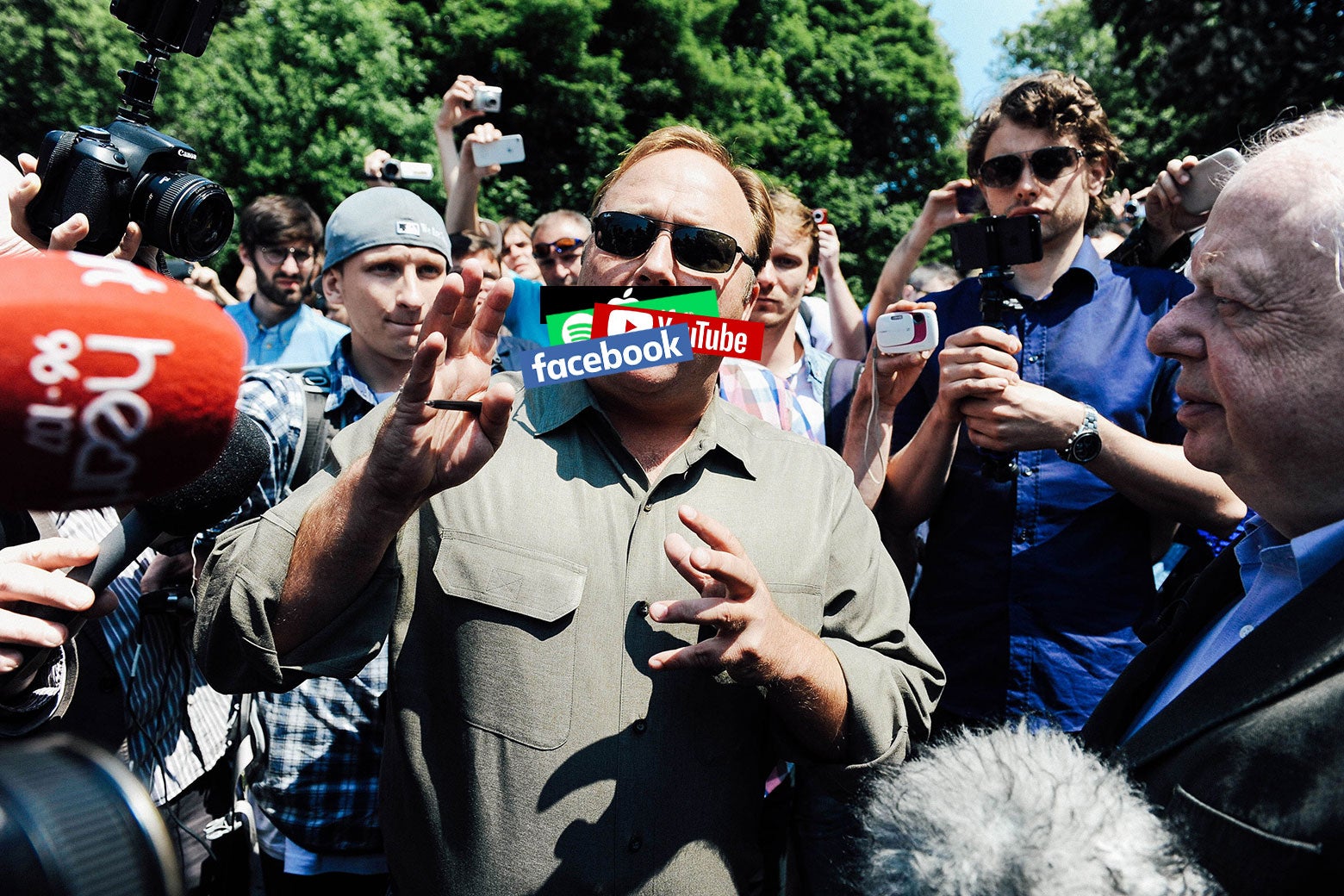 Alex Jones speaks to the media in Watford, Hertfordshire, England, in 2013. A series of social media logos have been digitally pasted over his mouth.