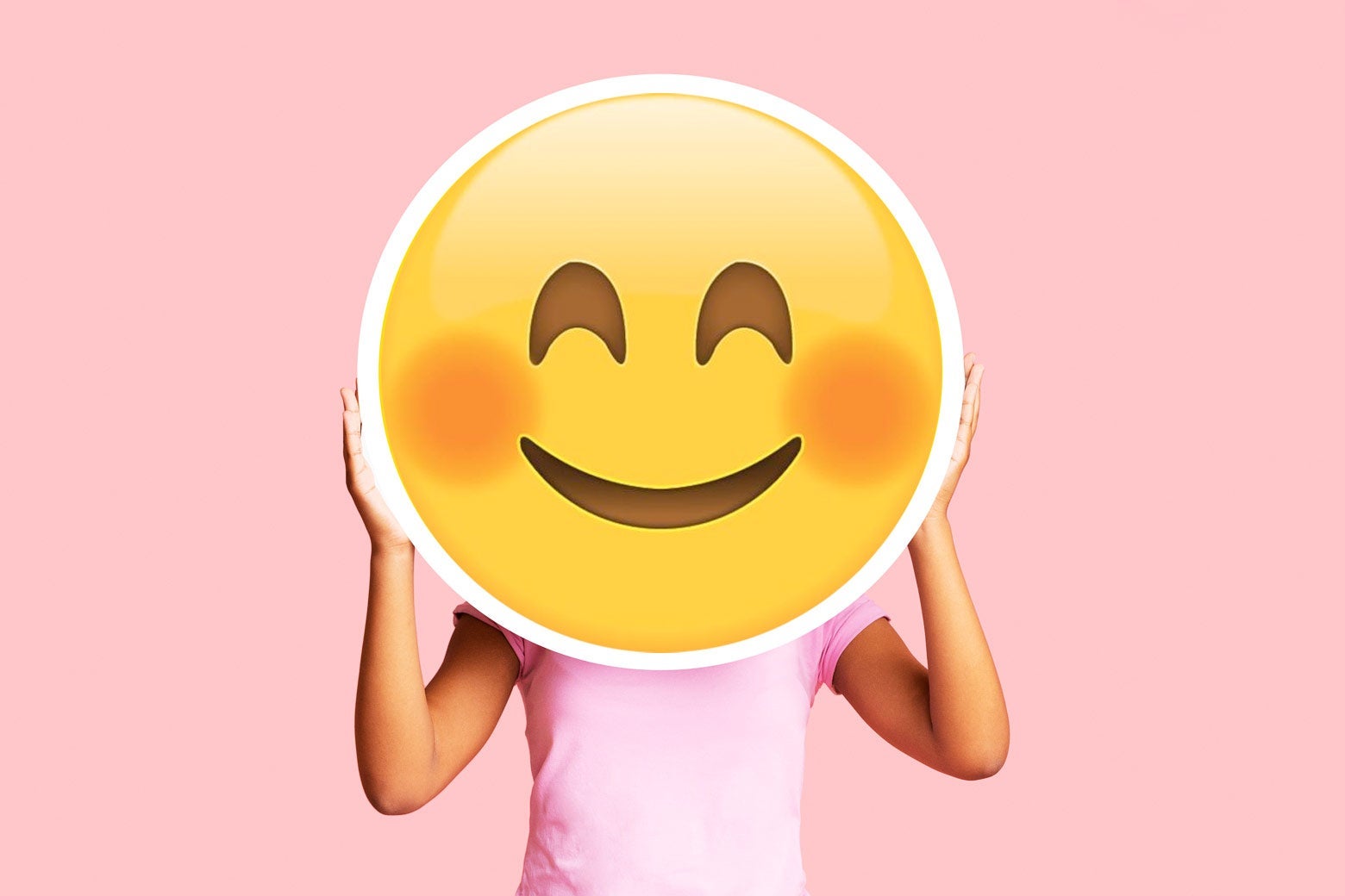 A woman holding a big blushing emoji over her face