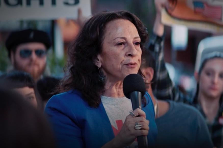 Maria Hinojosa stands in a crowd holding a microphone.