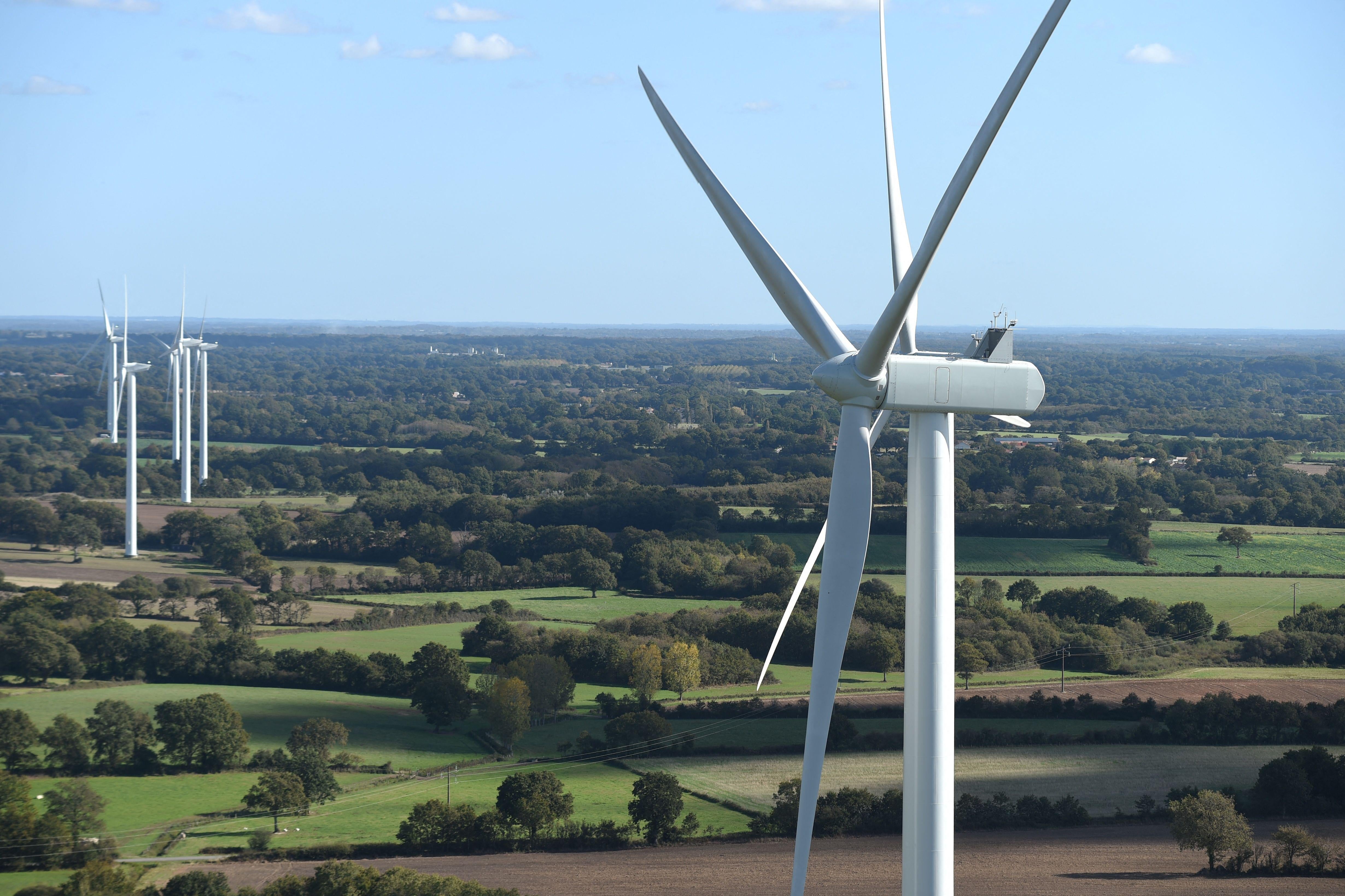 Wind turbines can be seen across a green landscape lush with trees.